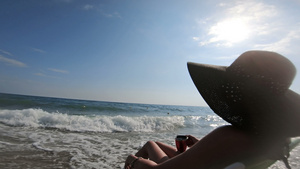 在海边海滩上坐着草帽的迷人女人享受海浪在岸上坠落时16秒视频