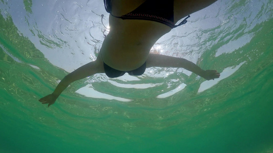 一位年轻女子在宁静的海水水面上游泳时在夏日阳光照耀视频