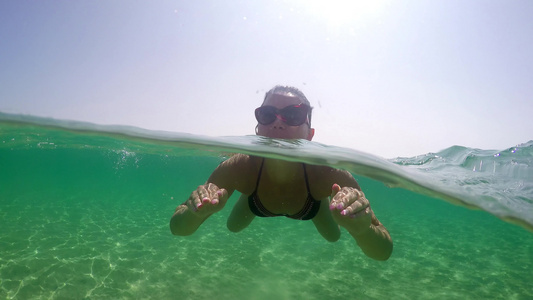 一位年轻女子在宁静的海水水面上游泳时在夏日阳光照耀视频