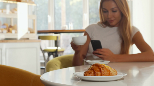 有选择性地关注美味的羊角面包妇女在咖啡店使用智能手机视频