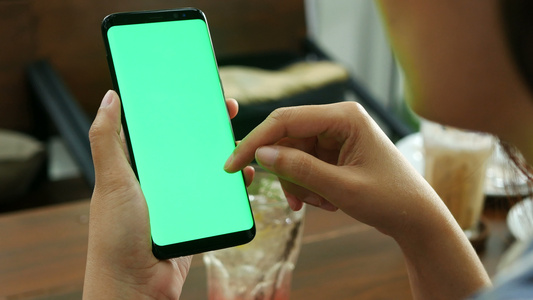 4K女人在咖啡店使用带有空白绿屏模型的移动智能手机视频