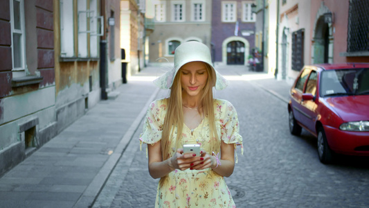 穿着白帽子的年轻女士走在老城街上用智能手机发短信她视频