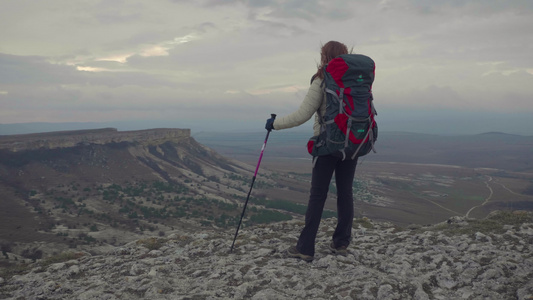 带着背包和徒步杆的年轻登山女青年站在岩石边缘稳定全拍视频