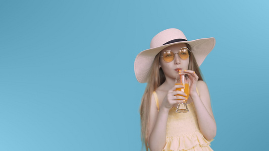 穿着黄色眼镜和帽子的年轻少女在蓝色屏幕上喝鸡尾酒视频