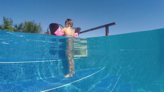 带着臂带的年轻女孩走出游泳池半水下风景慢动作视频