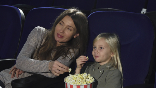 美丽的女人和她的小女儿在电影院吃爆米花看电影视频