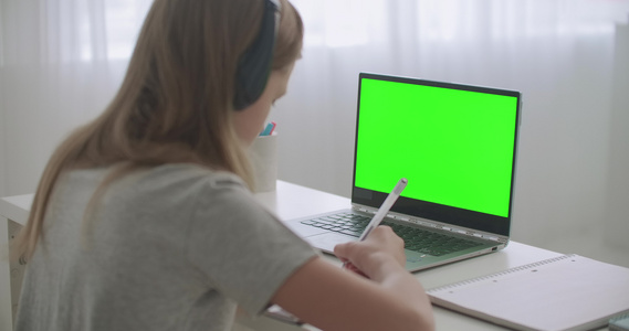 青少年女孩正在网上学习坐在笔记本电脑前的桌子上手持视频