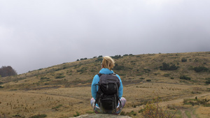穿着蓝色夹克的女性徒步旅行者背着背包坐在岩石上欣赏10秒视频