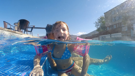 带着臂带的小女孩在游泳池使滑稽舌头向摄影机发出尖锐视频