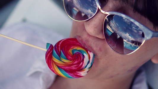 美丽的女孩带着太阳眼镜在海滩舔棒棒棒糖玩得开心视频