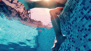 女人坐在游泳池边缘她的腿在游泳池水下风景26秒视频