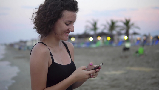 可爱的少女女孩在她的智能手机上发短信在空海滩上大笑视频