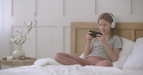 女孩在放学后用智能手机玩游戏独自坐在家中的床上童年时期视频