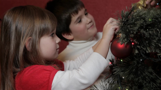小男孩在圣诞树上挂着装饰的弓视频