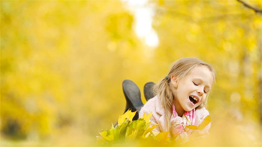 可爱的小女孩在秋天的黄色叶子花束的画像躺在树叶地毯视频