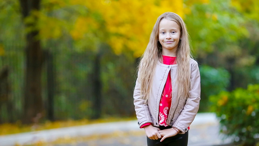 可爱小女孩的肖像在秋天倒在地上看着镜头和微笑视频