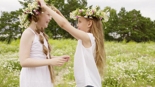 两个女孩戴着花环在夏日盛开的草地上玩耍快乐的女孩少年视频