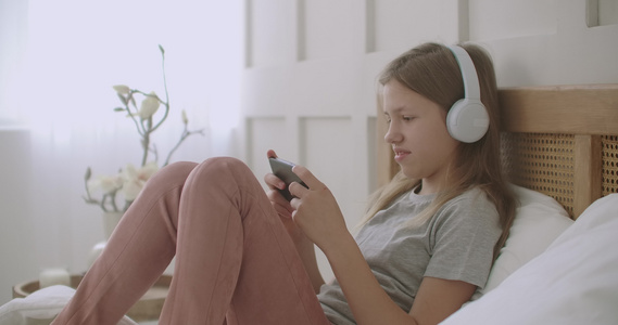 女学生呆在家里玩手机游戏躺在床上用耳机听音乐视频