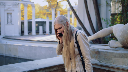 一个快乐的年轻女孩在城市秋季公园使用手机说话在城市视频