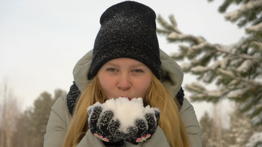 带着冬衣的快乐年轻女孩从双手中吹雪视频