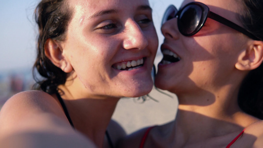两个美丽的姐妹的肖像笑着和做傻脸在沙滩上的相机上视频