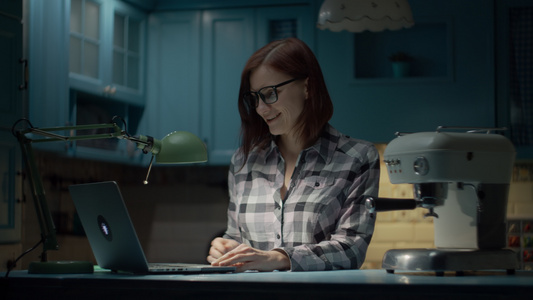30多岁的年轻女子戴着眼镜晚上在蓝色厨房的家里用笔记本电脑视频