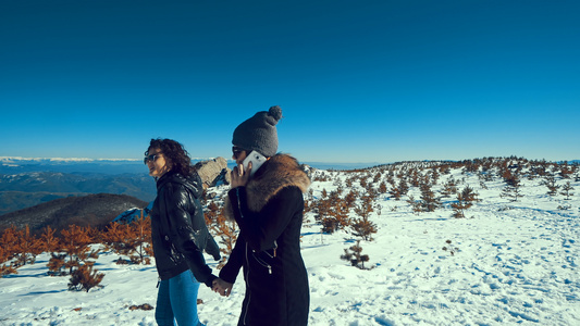 两个少女在雪雪上走动手牵手笑着用智能手机说话视频