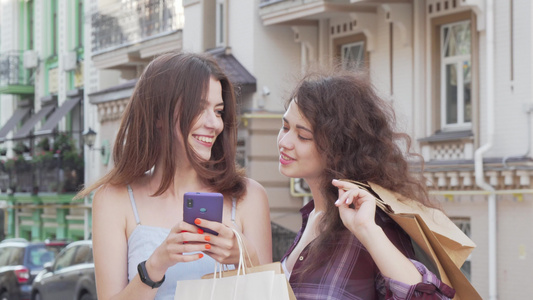 两位快乐的年轻女性在户外智能手机上浏览网络视频