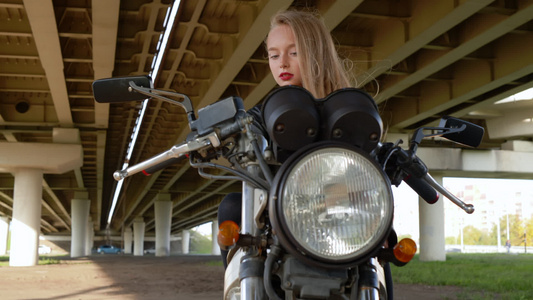 穿着皮夹克的年轻骑自行车的女孩骑着黑色摩托车在车桥下视频