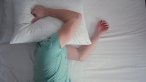 年轻人躺在床上熟睡着他在睡眠中受到干扰用枕头盖住自己22秒视频