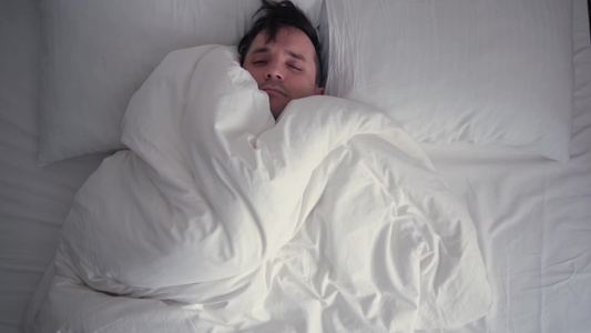 年轻人用厚厚的毯子裹着头睡得很熟冬天热白色床上用品视频
