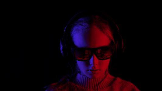 微笑的女孩戴着耳机和黑色太阳镜在带红色和蓝色背光的视频