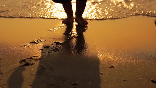 婴儿赤脚步行在海滩沙滩上海日落浪冲洗沙子缓慢运动视频