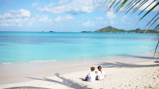 沙滩上的两个小女孩快乐的孩子们坐在热带海滩的棕榈树视频