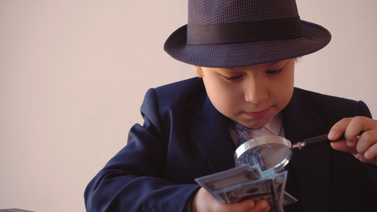 男孩看起来像一个商人在帽子和西装正在寻找美元与放大镜视频