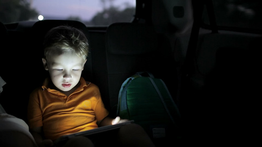 小男孩在夜间乘车旅行时使用平板电脑视频