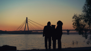 父母孩子站在河桥景观一起看日落的剪影18秒视频