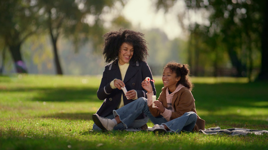 快乐的女儿吹肥皂泡泡坐在阳光明媚的公园里视频