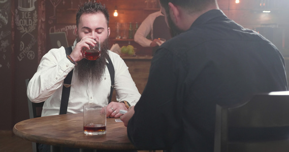 两个大胡子男人在一个酒吧喝酒社交和开始玩牌游戏视频