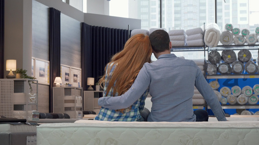 坐在家具店新床铺的一对夫妇抱抱的后视镜头视频