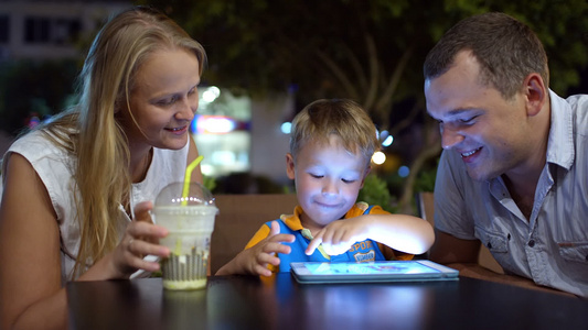 男孩与父母一起坐在咖啡馆的平板电脑上视频