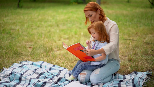 快乐的年轻母亲与女儿一起在户外阅读视频