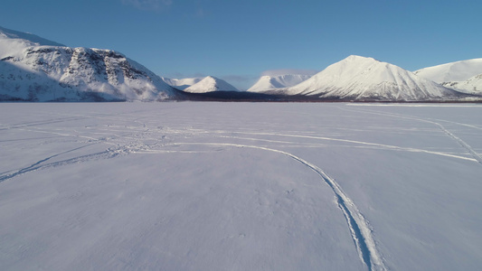 在冬季阳光明媚的日子里低角度无人机向前飞越雪湖到山脉视频