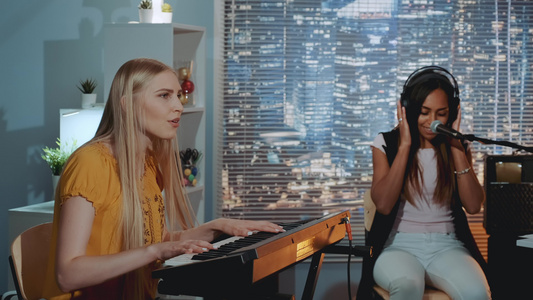 漂亮的女孩唱着一首歌而其中一人在家排练时玩键盘视频