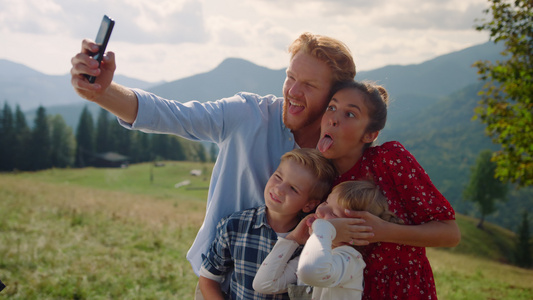 顽皮的家庭在智能手机站在山坡上做鬼脸自拍视频