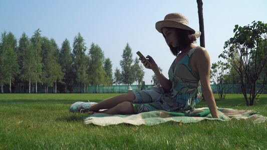 黑发姑娘坐在公园的毯子上在电话里收到一条信息笑声视频
