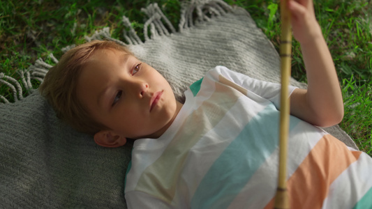 特写心烦意乱的男孩独自检查躺在绿草上的木制羽毛球拍视频