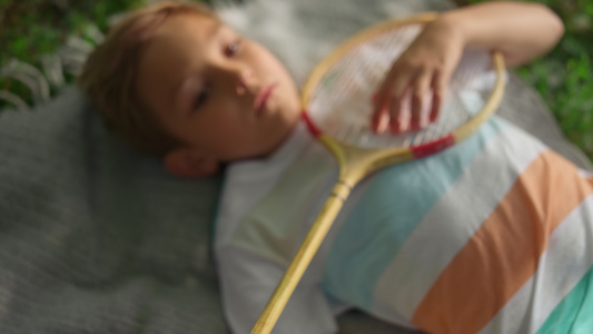 特写疲倦的男孩躺在毯子在夏季公园检查羽毛球球拍网视频