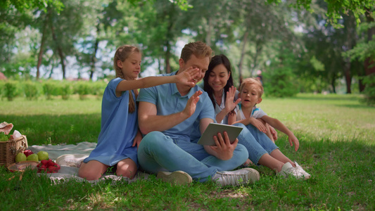 微笑的家人挥手在夏日使用平板电脑在大自然中交流视频