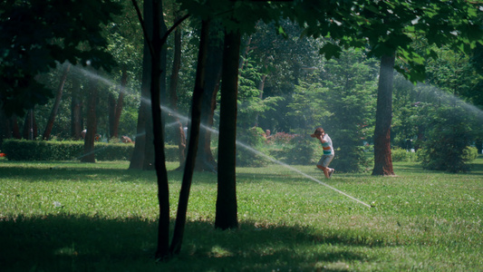 嬉戏的小男孩自来水洒在绿色公园里耳朵不被溅起视频